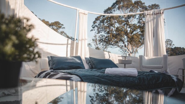 Una cama con dosel, almohadas y una silla blanca.