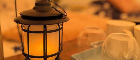 Un farol negro con revestimiento de vidrio, sobre una bandeja que contiene un recipiente de vidrio transparente y un objeto blanco, posiblemente un candelabro, sobre una superficie de madera.