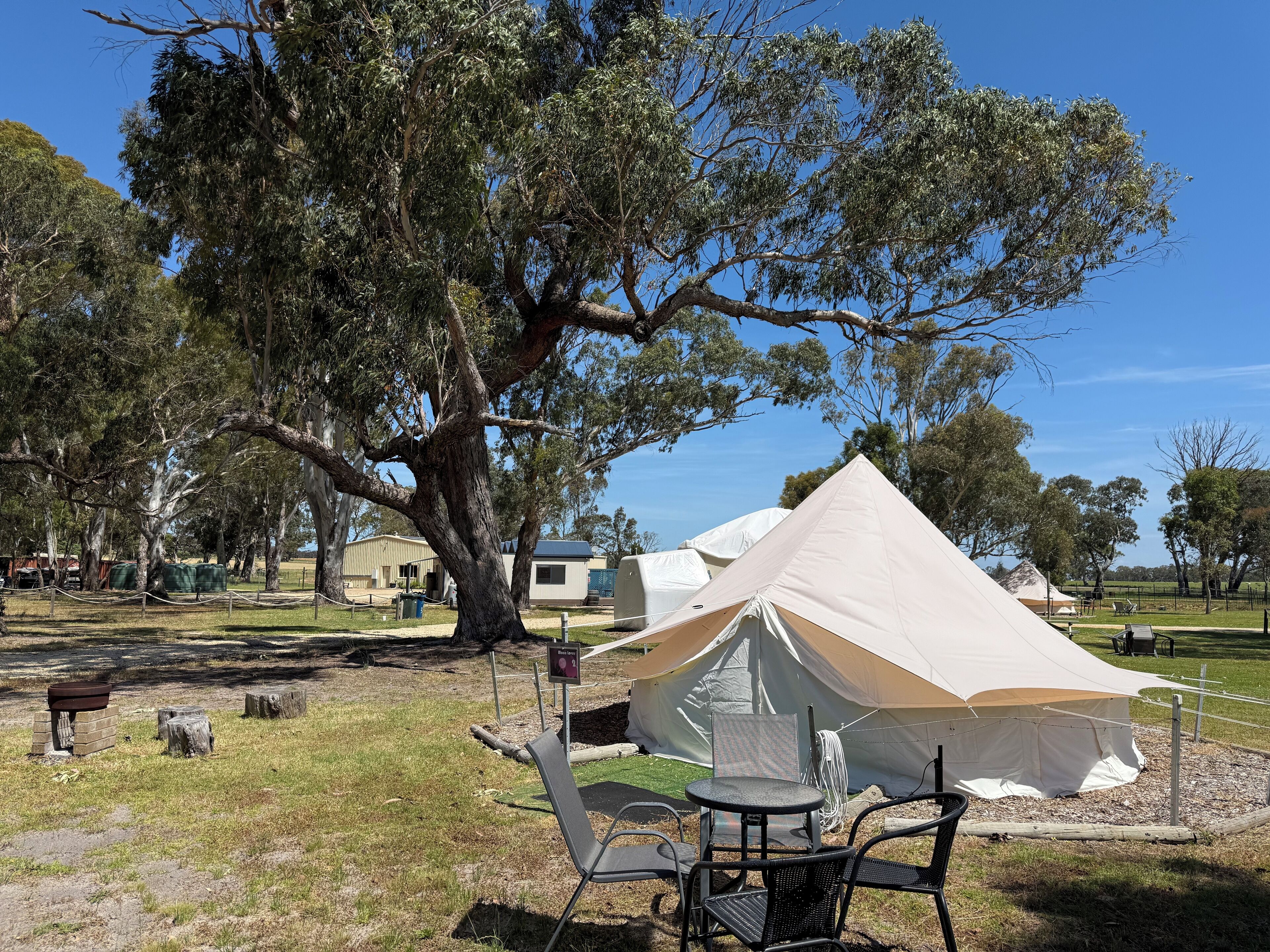 A campsite with a large tent, picnic table, and chairs.