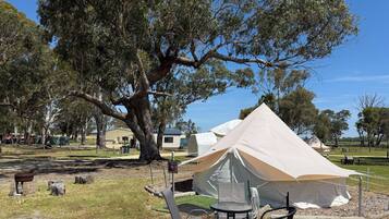 A campsite with a large tent, picnic table, and chairs.