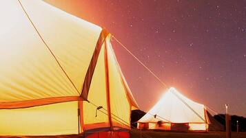 A series of tents set up in a grassy field under a starry night sky.