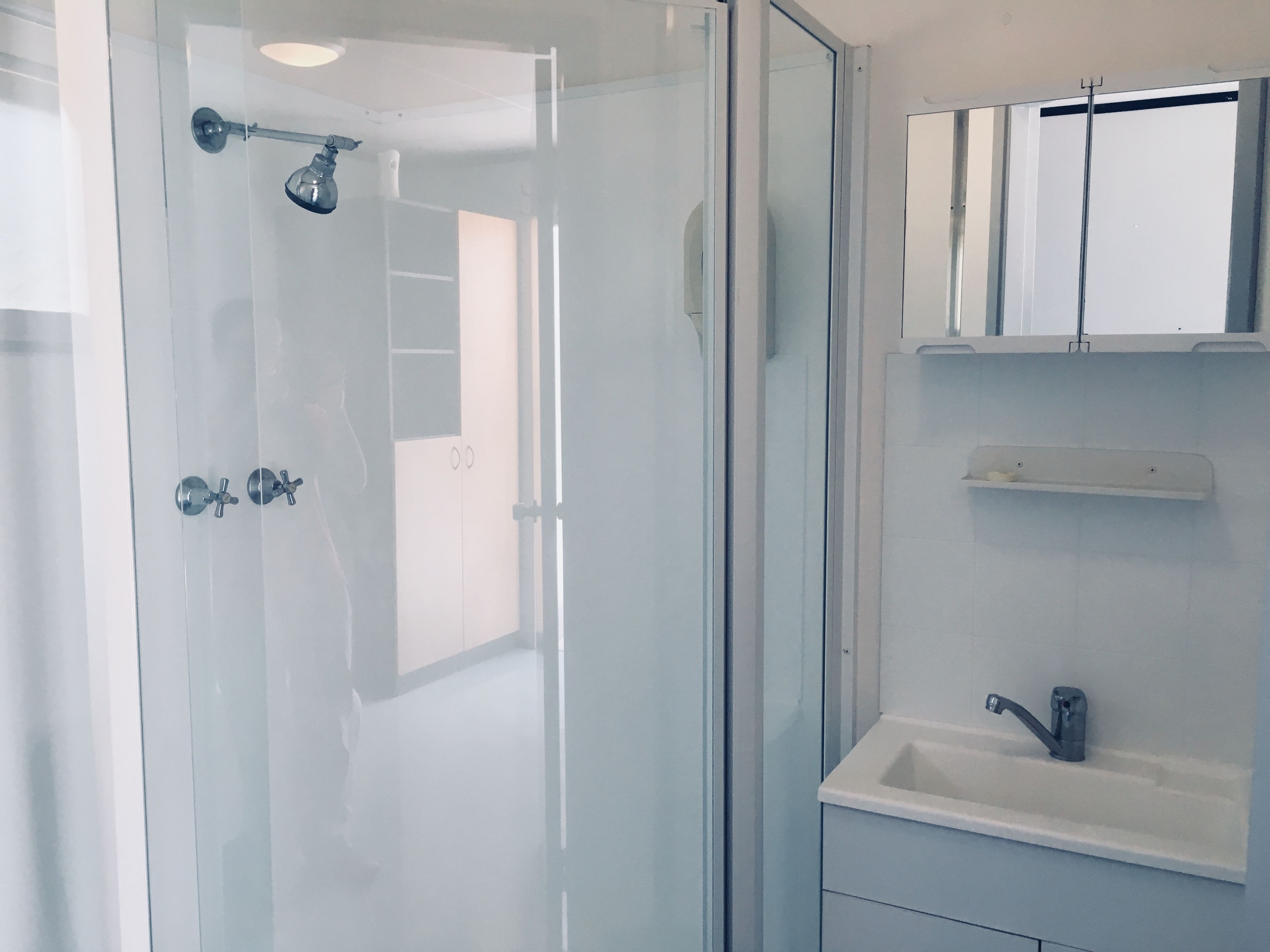 Un bagno moderno con cabina doccia in vetro, lavandino bianco e specchio sopra il lavandino.
