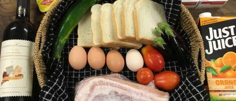A basket containing bread, eggs, tomatoes, a cucumber, a piece of meat, and a bottle of wine.