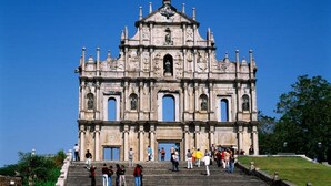 A large, historic building with multiple arches and a central entrance, surrounded by a grassy area and steps leading up to it. - Grand Harbour Hotel (Macau)