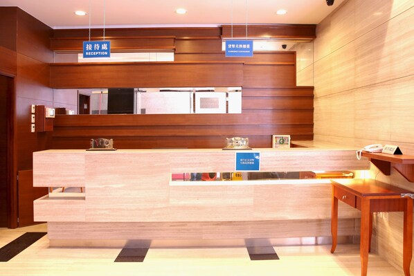 A reception desk with a wooden finish, a telephone, and a sign indicating a currency exchange service. - Grand Harbour Hotel (Macau)