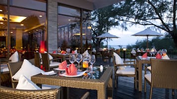 Un área de comedor al aire libre con mobiliario de mimbre, mesas de vidrio y sombrillas.