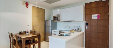Una cocina compacta con una mesa de comedor, sillas de madera, un microondas, un lavabo y una puerta de madera.