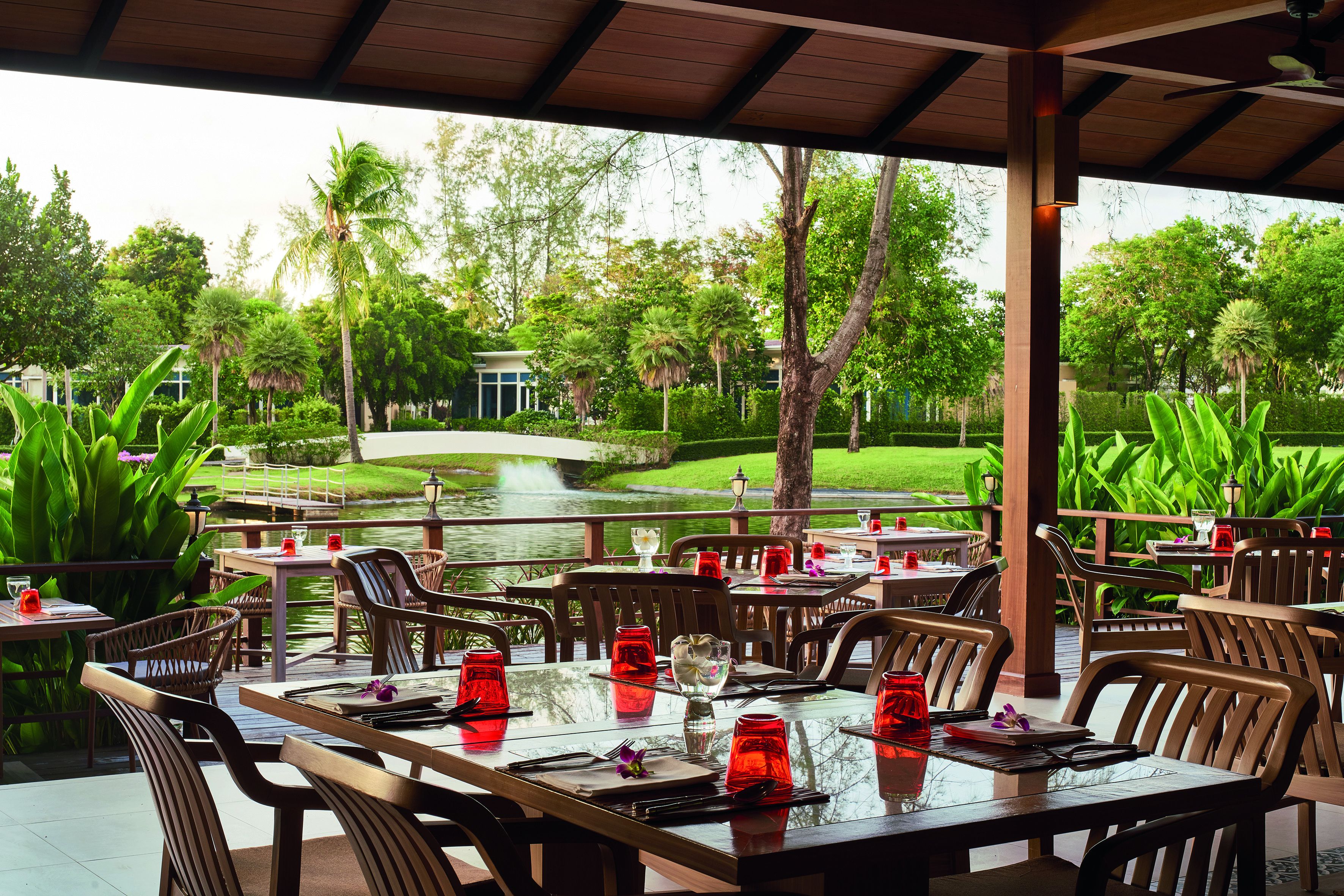 Un espace extérieur aménagé pour les repas, avec des tables et des chaises, un bassin et de la verdure en arrière-plan.