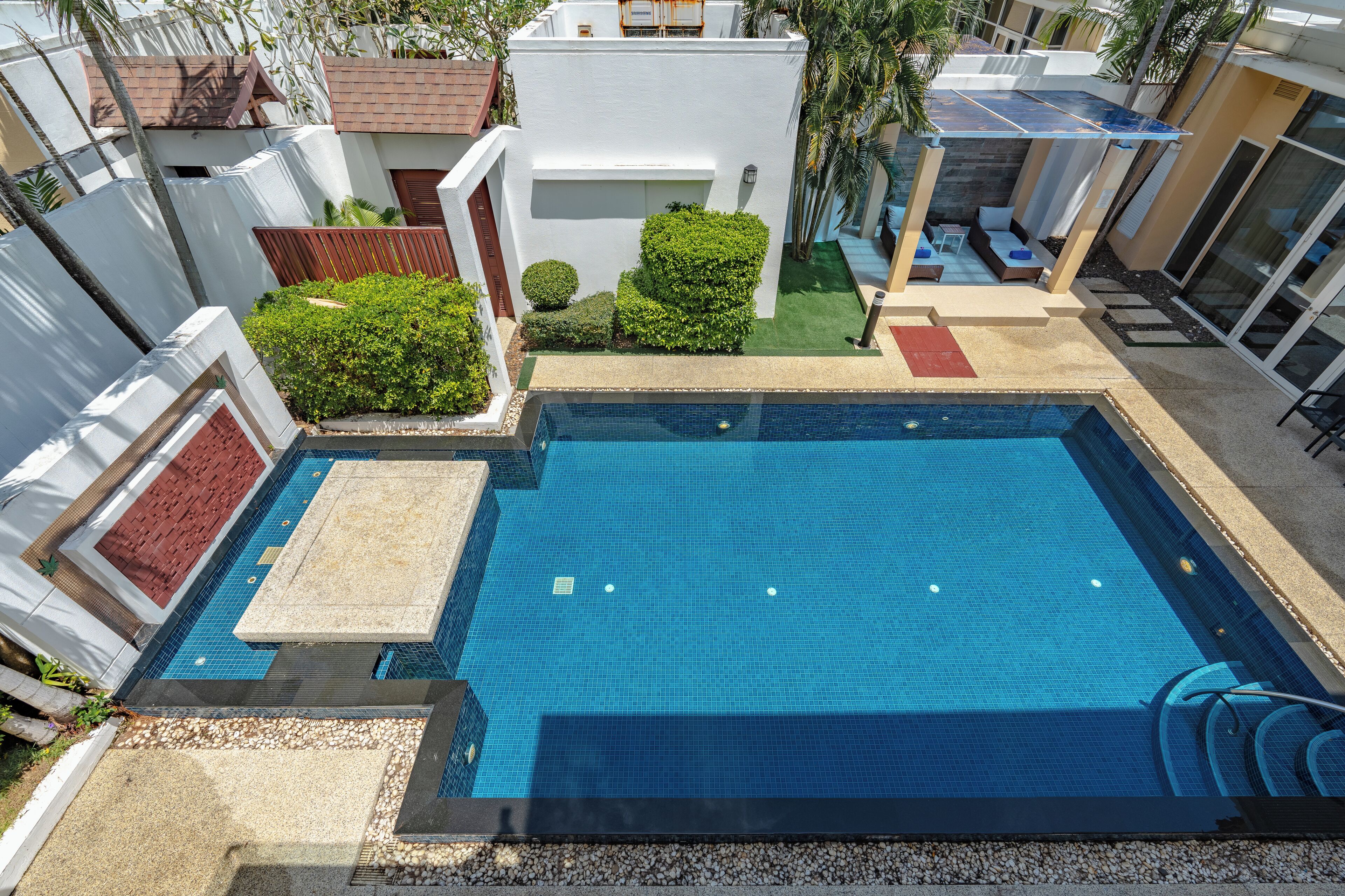 Une piscine située sur le toit, avec une eau d’un bleu limpide, entourée d’un bâtiment blanc et de verdure.