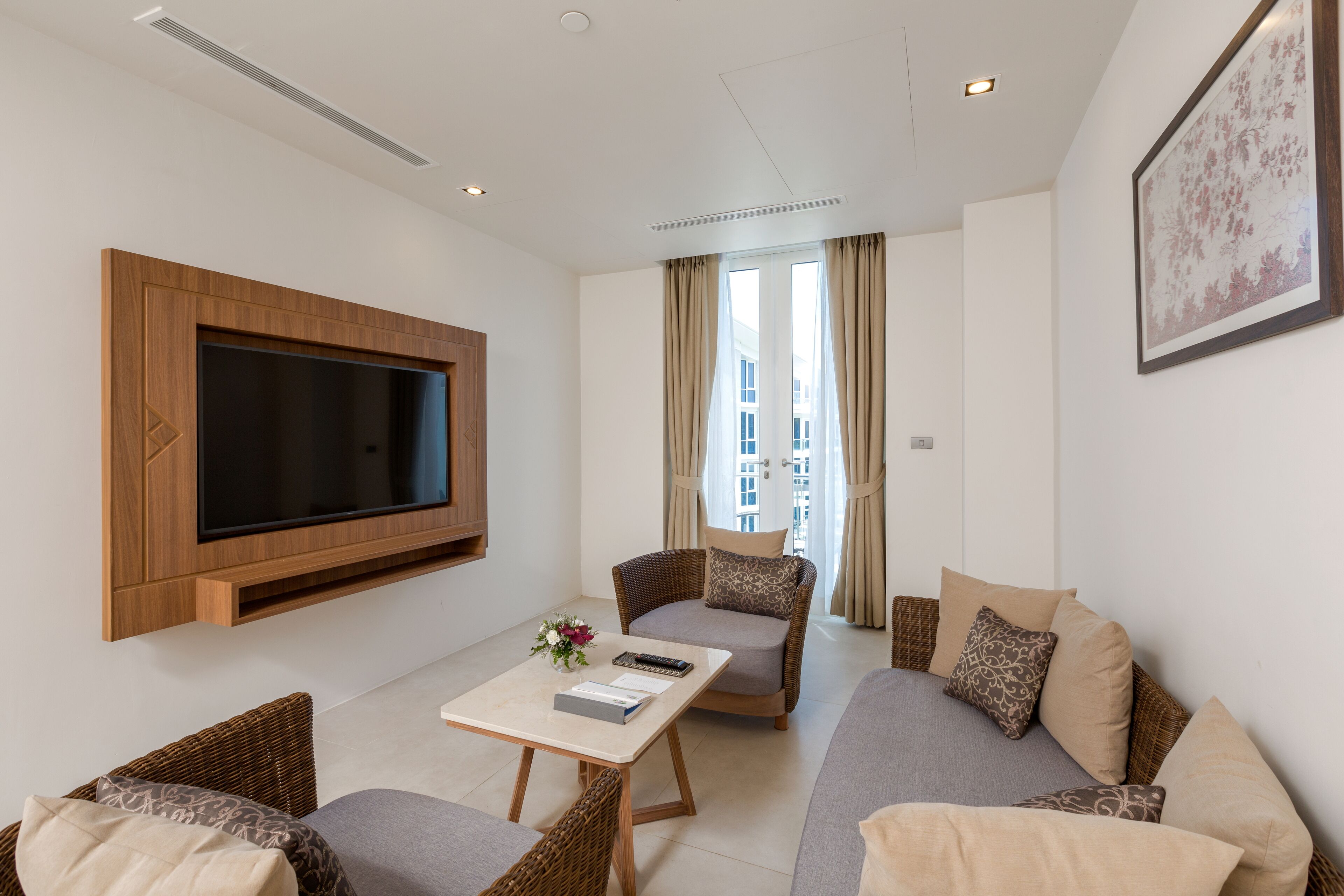 A modern living room with a flat-screen TV mounted on the wall, a sofa, a coffee table, and a wicker chair.