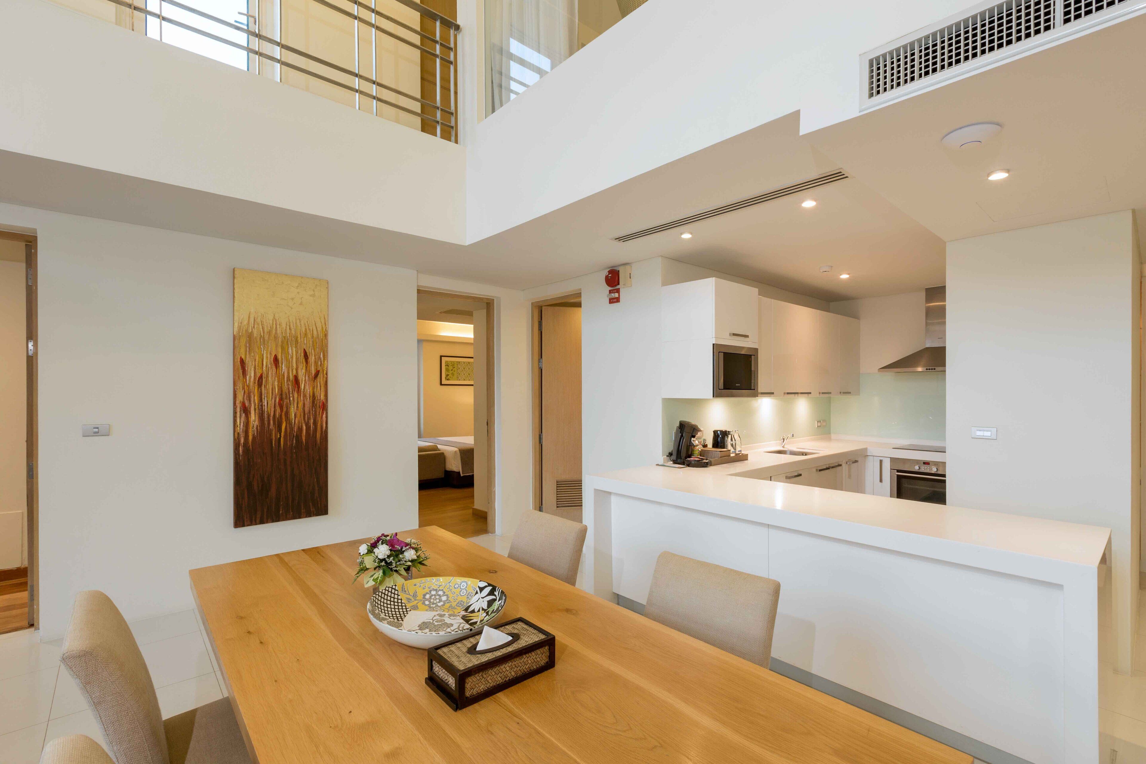 Una cocina moderna con armarios blancos, una isla central y un comedor con mesa y sillas de madera.