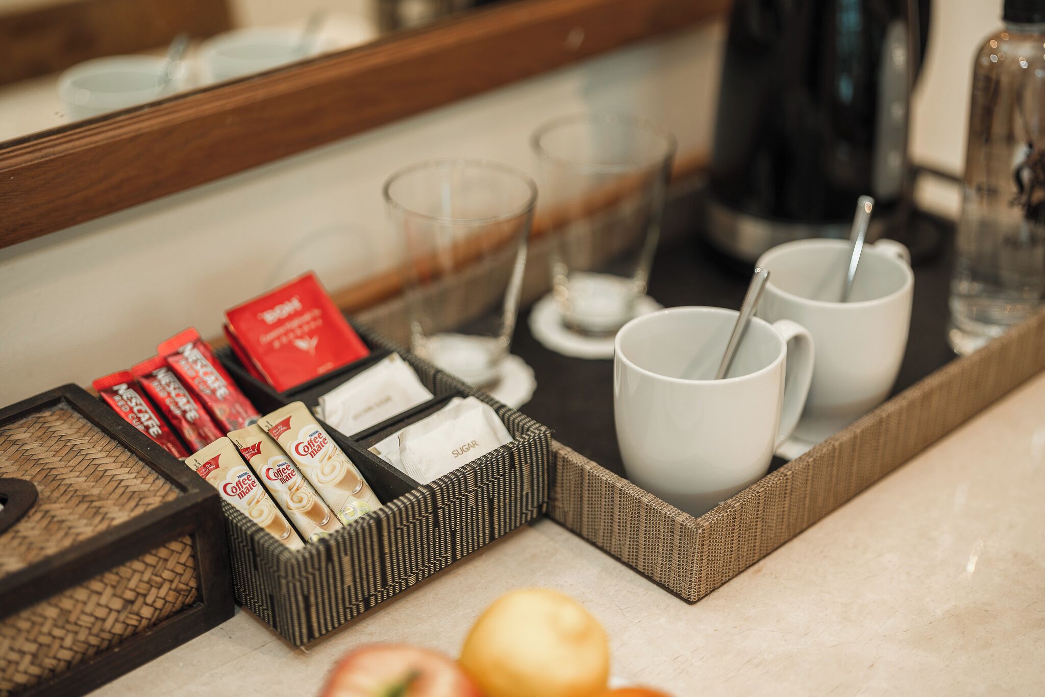 A tray with coffee packets, sugar packets, and two white mugs with spoons, placed on a marble countertop.