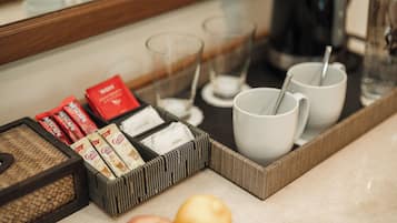 A tray with coffee packets, sugar packets, and two white mugs with spoons, placed on a marble countertop.