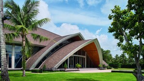 A modern building with a curved roof and large windows, surrounded by well-maintained grass and palm trees.