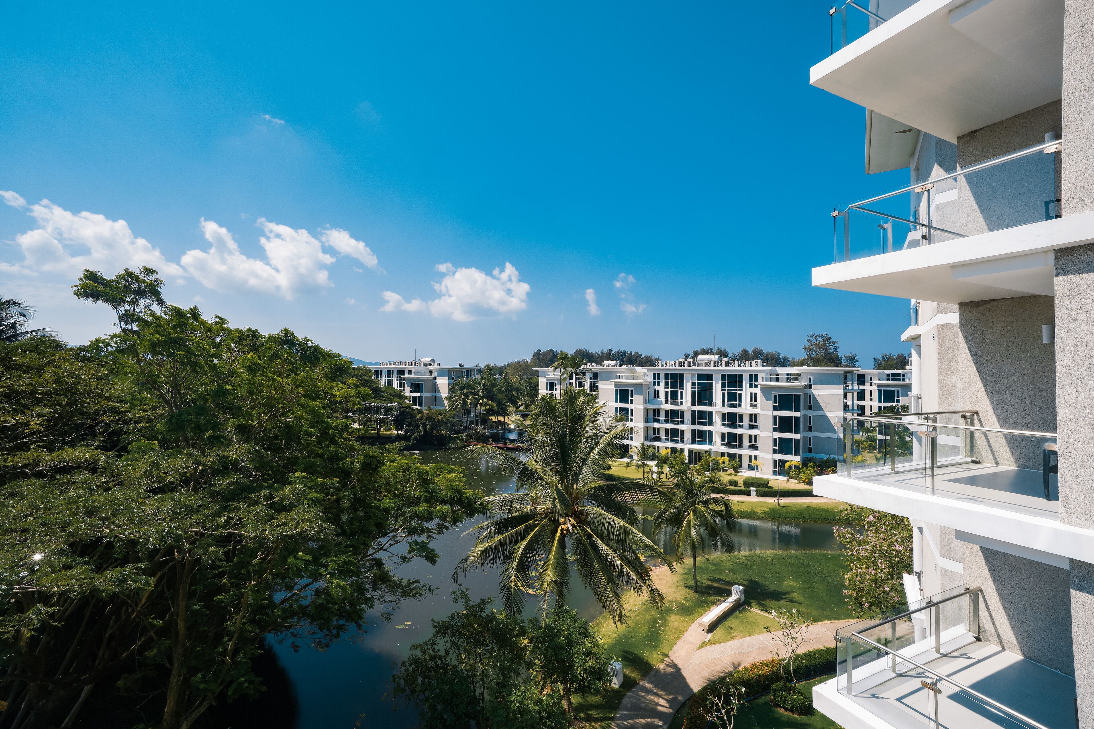 A modern building with multiple balconies overlooking a water body and lush greenery.