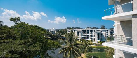 A modern building with multiple balconies overlooking a water body and lush greenery.