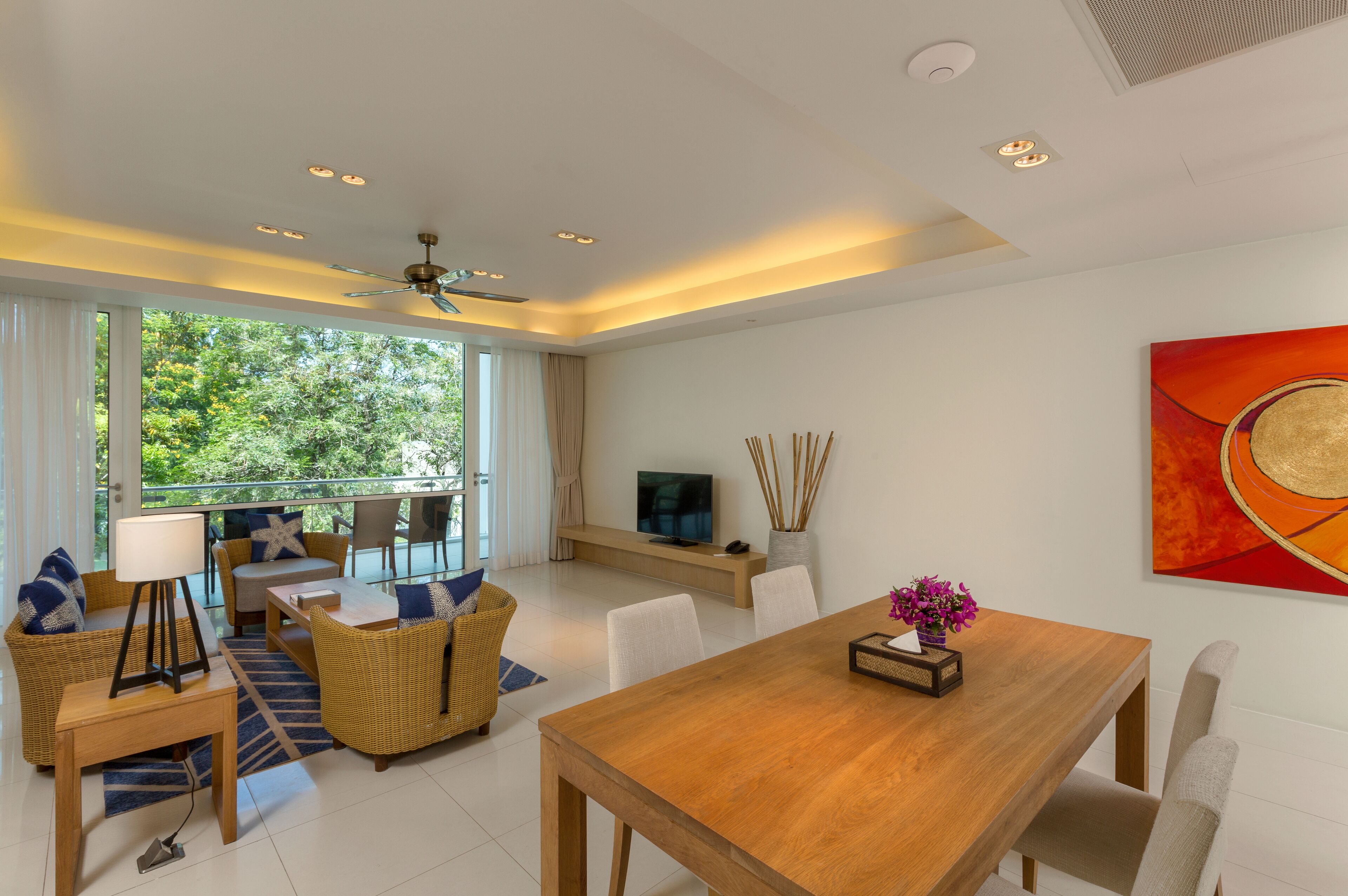 Una sala moderna con una mesa de comedor de madera, asientos cómodos, un televisor y un ventanal con vistas a la vegetación.