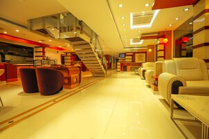 Vestíbulo de hotel con escalera, zona de estar, mostrador de recepción y una pantalla de televisión.