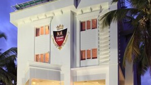 Un hotel moderno con un llamativo logotipo con forma de corona, amplias ventanas de vidrio y un área de entrada pavimentada.