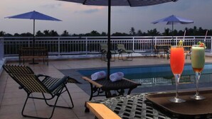 Zona de piscina con sillones de descanso, sombrillas y una mesa con bebidas.