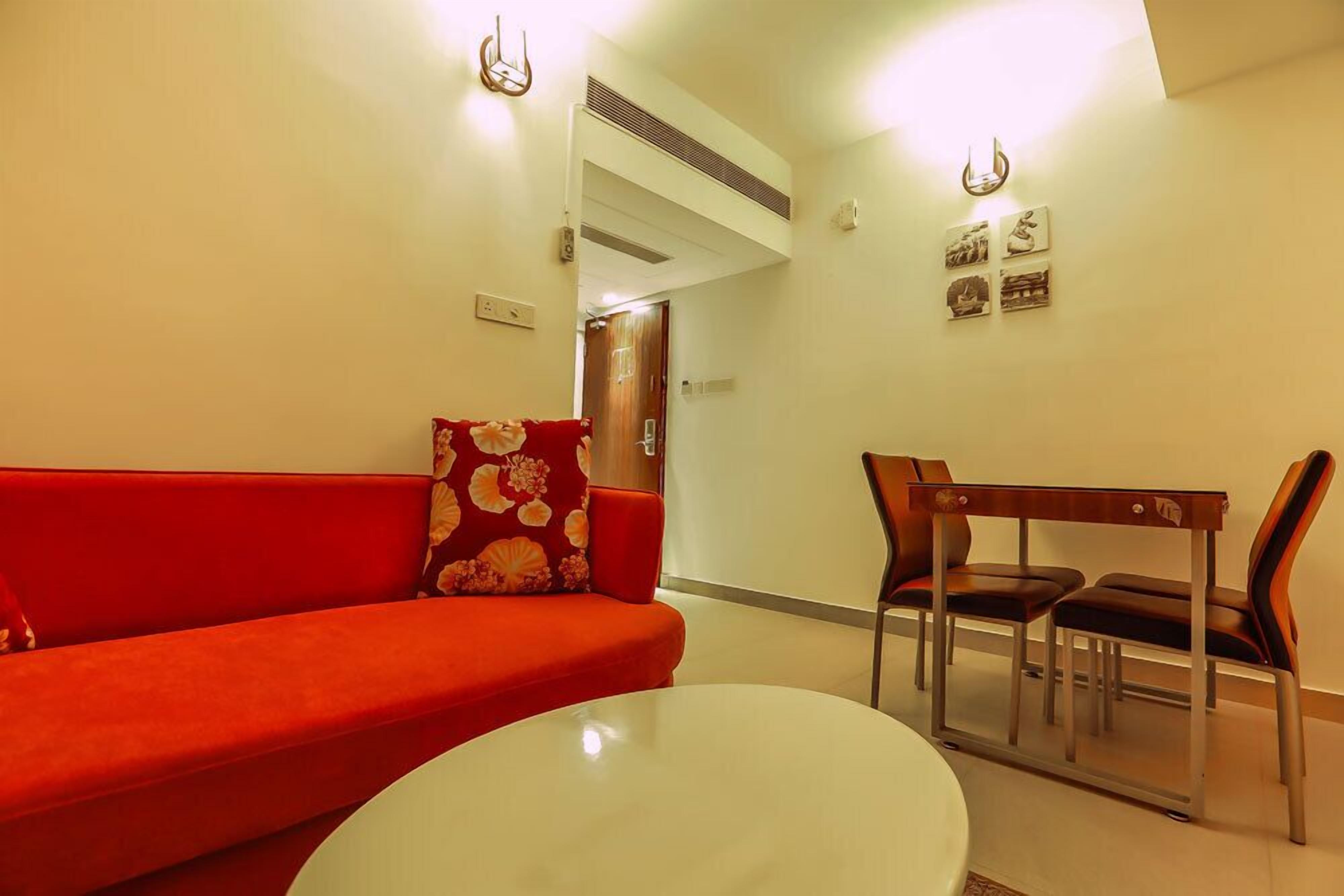 A modern living room with a red sofa, a round white table, and a wooden dining table with chairs.
