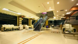 A spacious lobby with a central staircase, seating areas, and a reception desk. - NM Royale County (Kanayannur)
