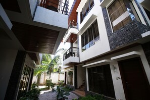 Un edificio residencial de varios pisos con balcones, un camino de piedra y un pequeño jardín.