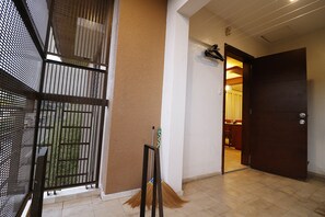 A hallway with a closed door, a broom leaning against the wall, and a mesh screen on the left.