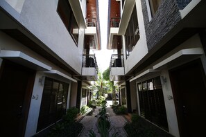 Un couloir étroit doté de balcons, un jardin central et une façade d’immeuble présentant un mélange de matériaux.