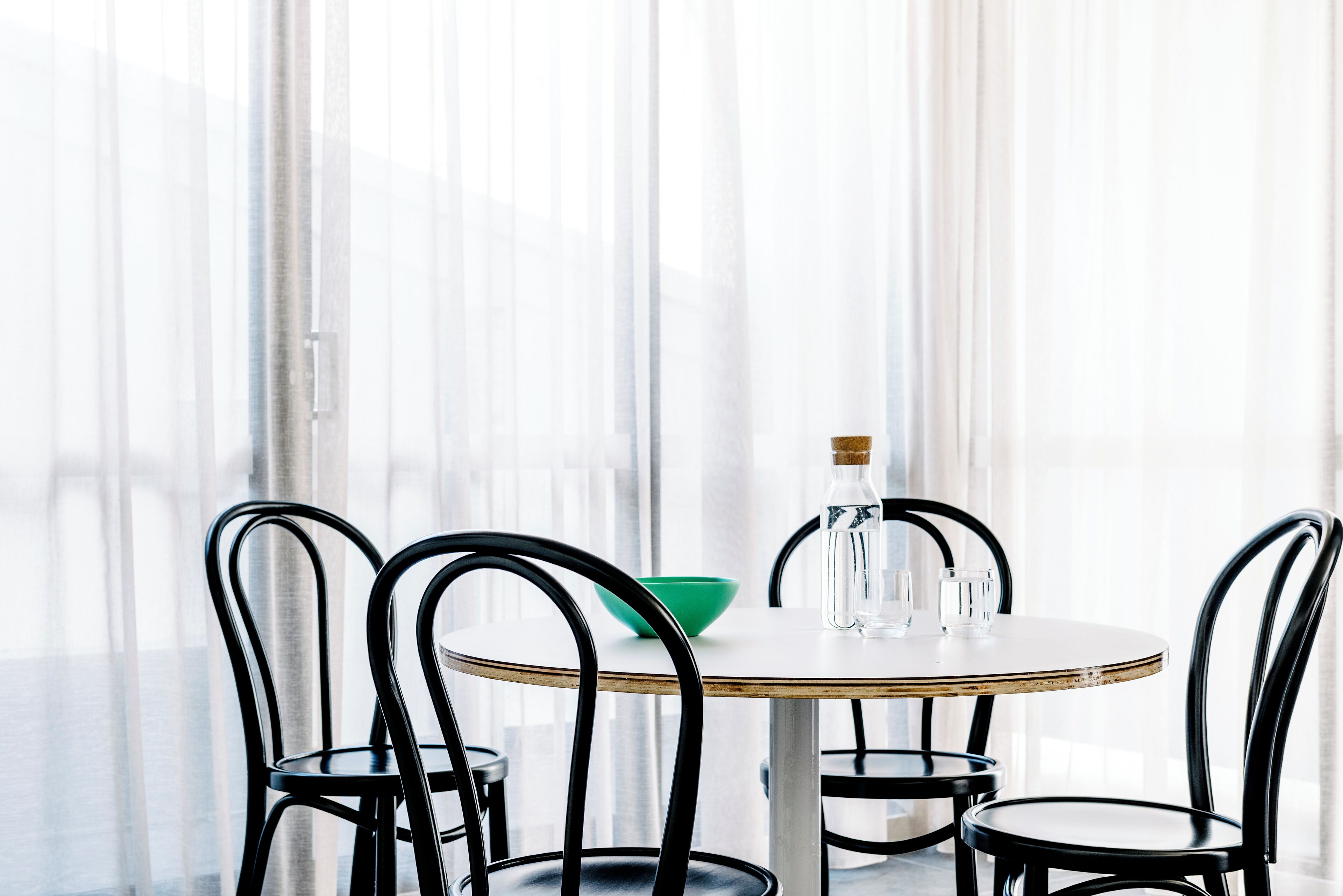 Une table de salle à manger ronde, accompagnée de quatre chaises noires, d’un saladier vert, d’une bouteille en verre et d’un verre.