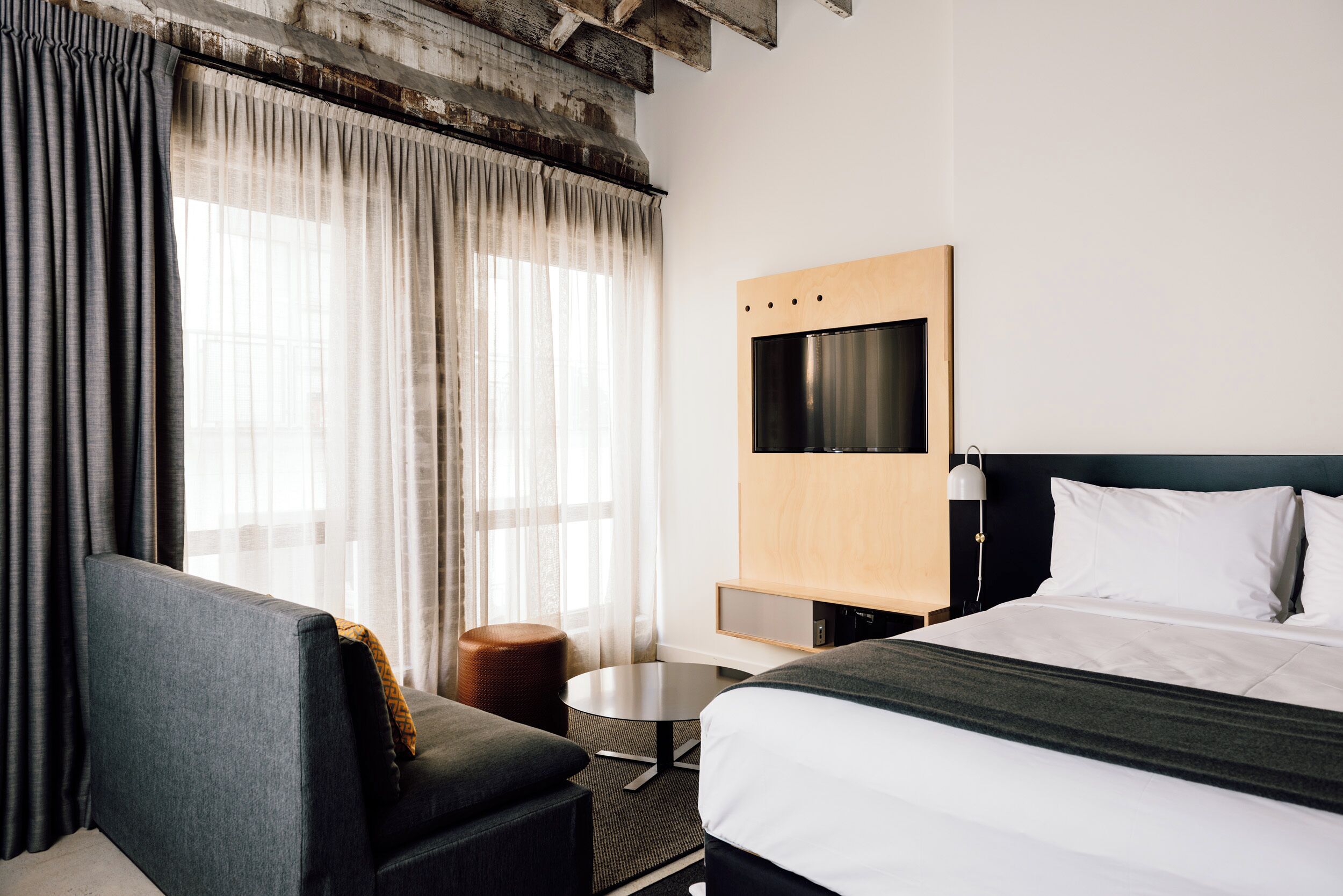 Une chambre d’hôtel avec un lit, un canapé, une petite table ronde, un téléviseur fixé au mur et une fenêtre avec des rideaux.