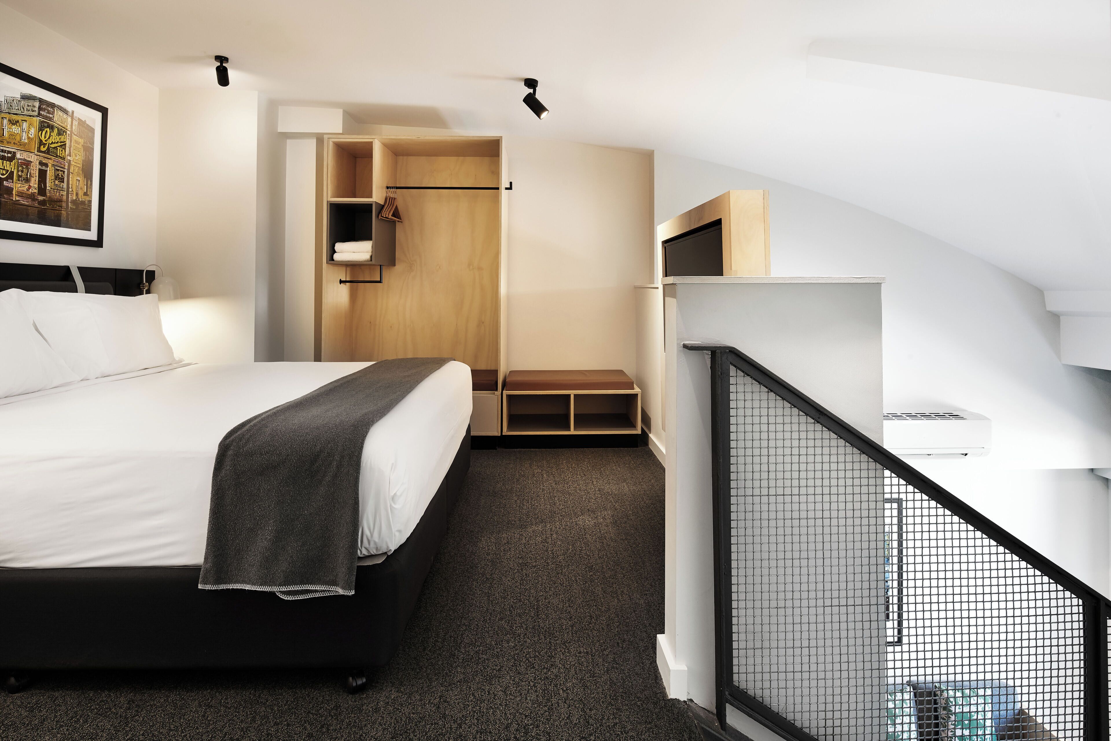 A modern hotel room with a large bed, a built-in desk, a small seating area, and a view of the city through the window.