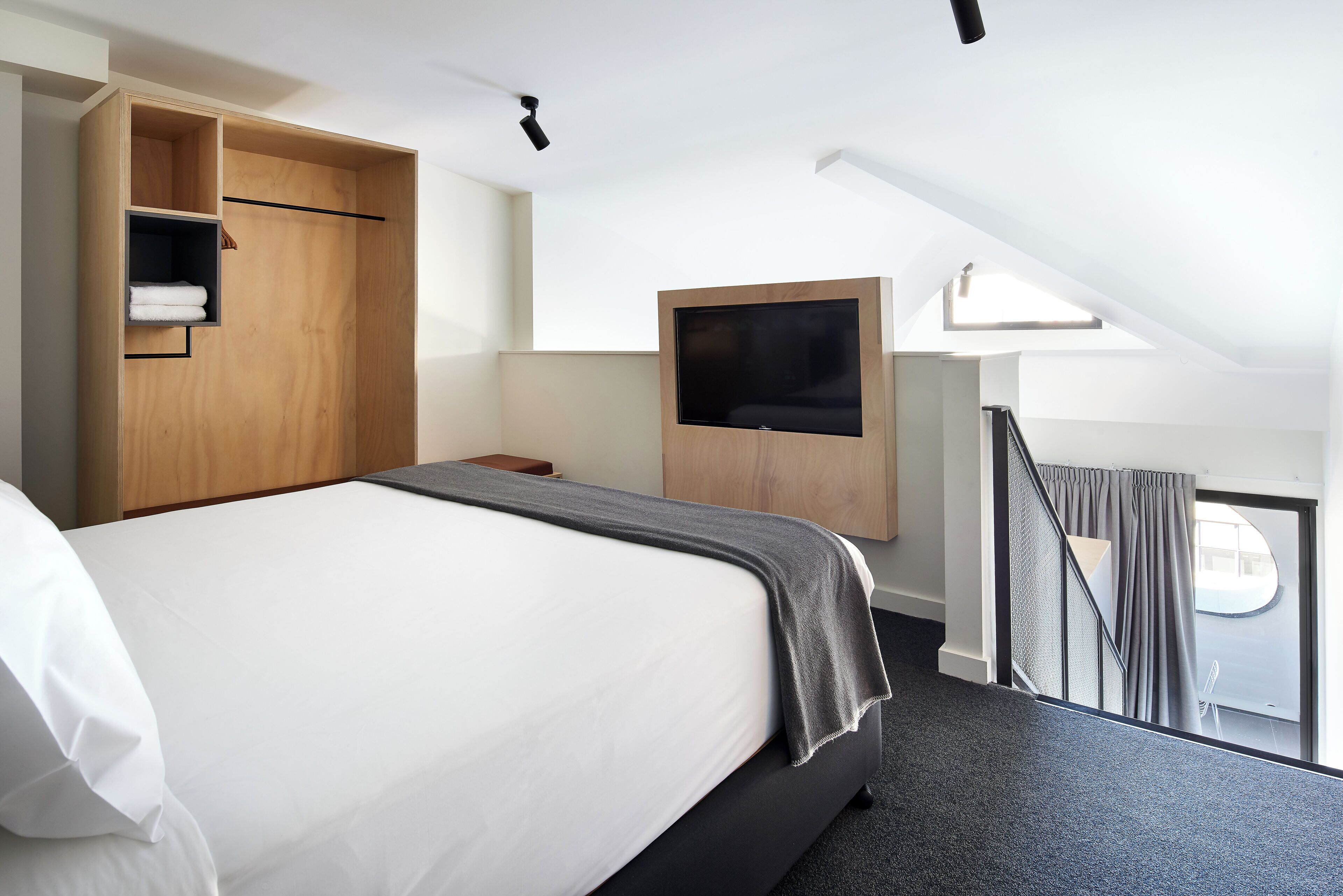Een moderne hotelkamer met een groot bed, een houten garderobe, een flatscreen televisie aan de muur en uitzicht door een raam.