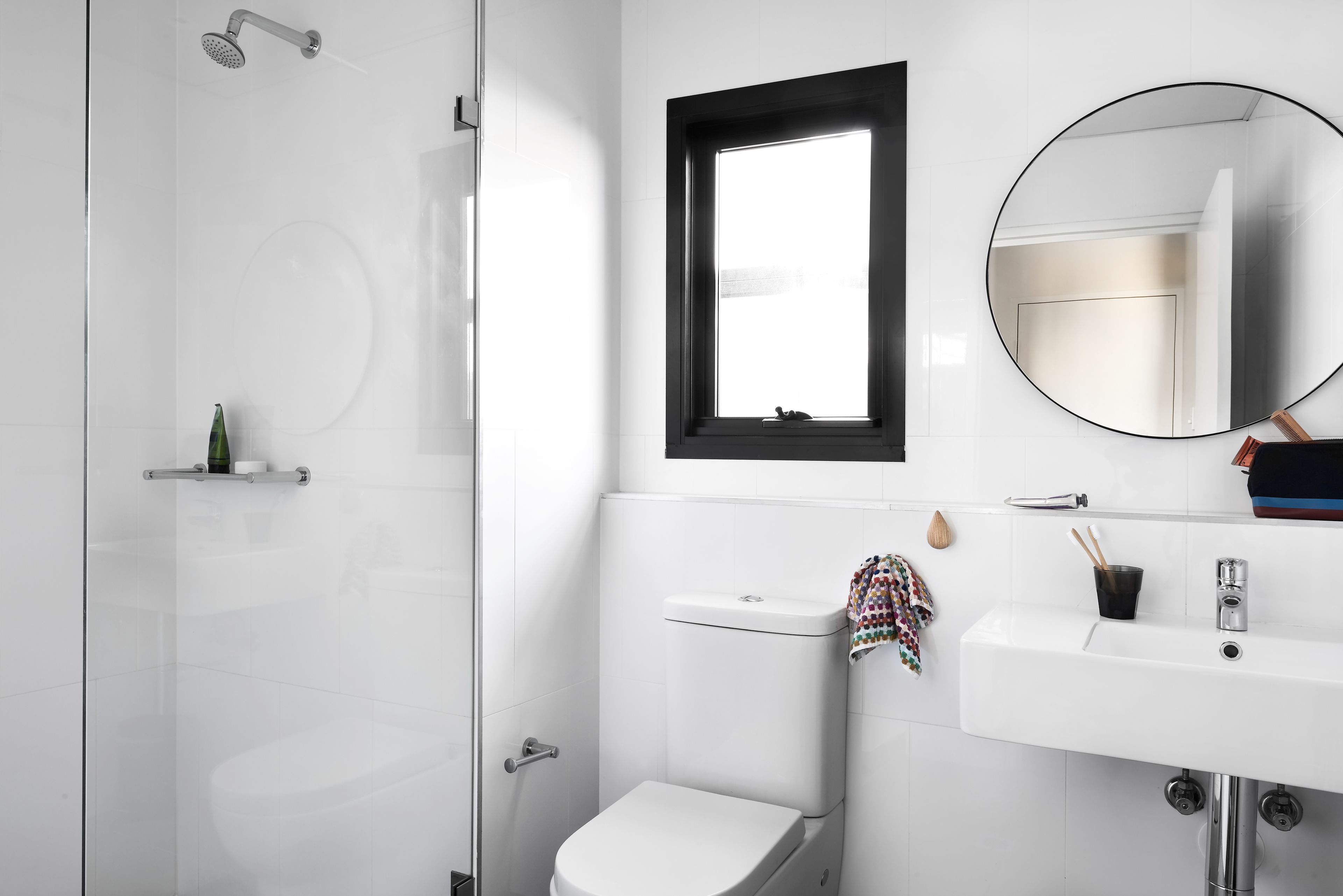 A modern bathroom with a glass shower enclosure, a toilet, a sink with a mirror, and a window above the sink.
