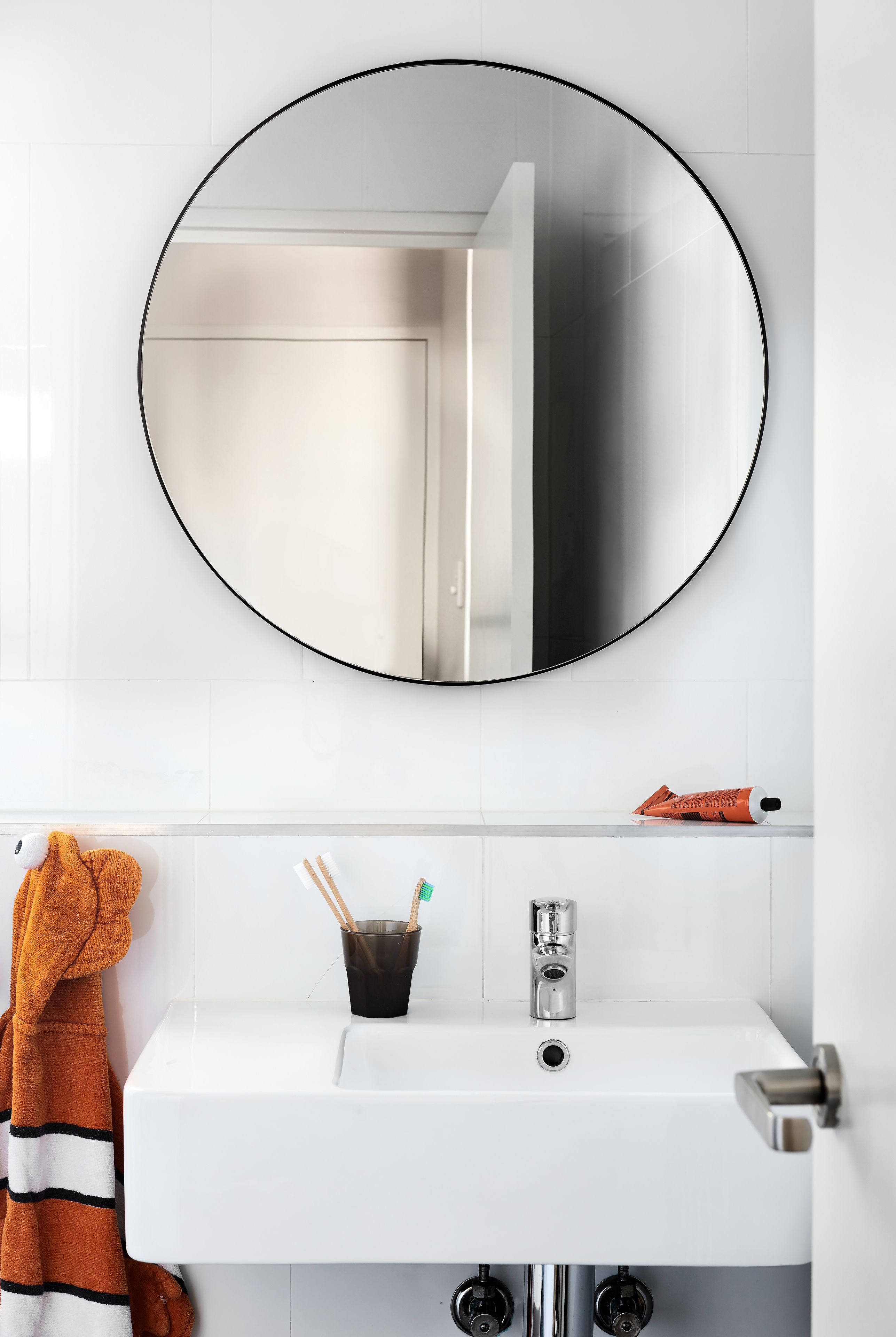 Een badkamer met een witte wasbak, een ronde spiegel en een handdoekrek met een gestreepte handdoek.