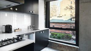 A modern kitchen with a gas stove, a dishwasher, and a window overlooking a brick building. - Veriu Broadway (Ultimo)