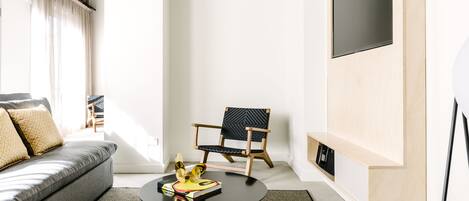 A modern living room with a sofa, a round coffee table, a wooden chair, and a TV mounted on the wall.