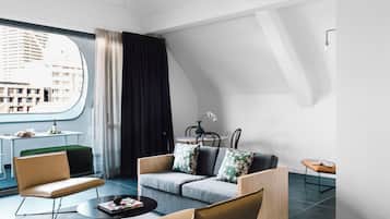 Ein modernes Wohnzimmer mit einer Couch, Sesseln, einem Couchtisch und Blick auf eine Skyline durch ein großes Fenster.