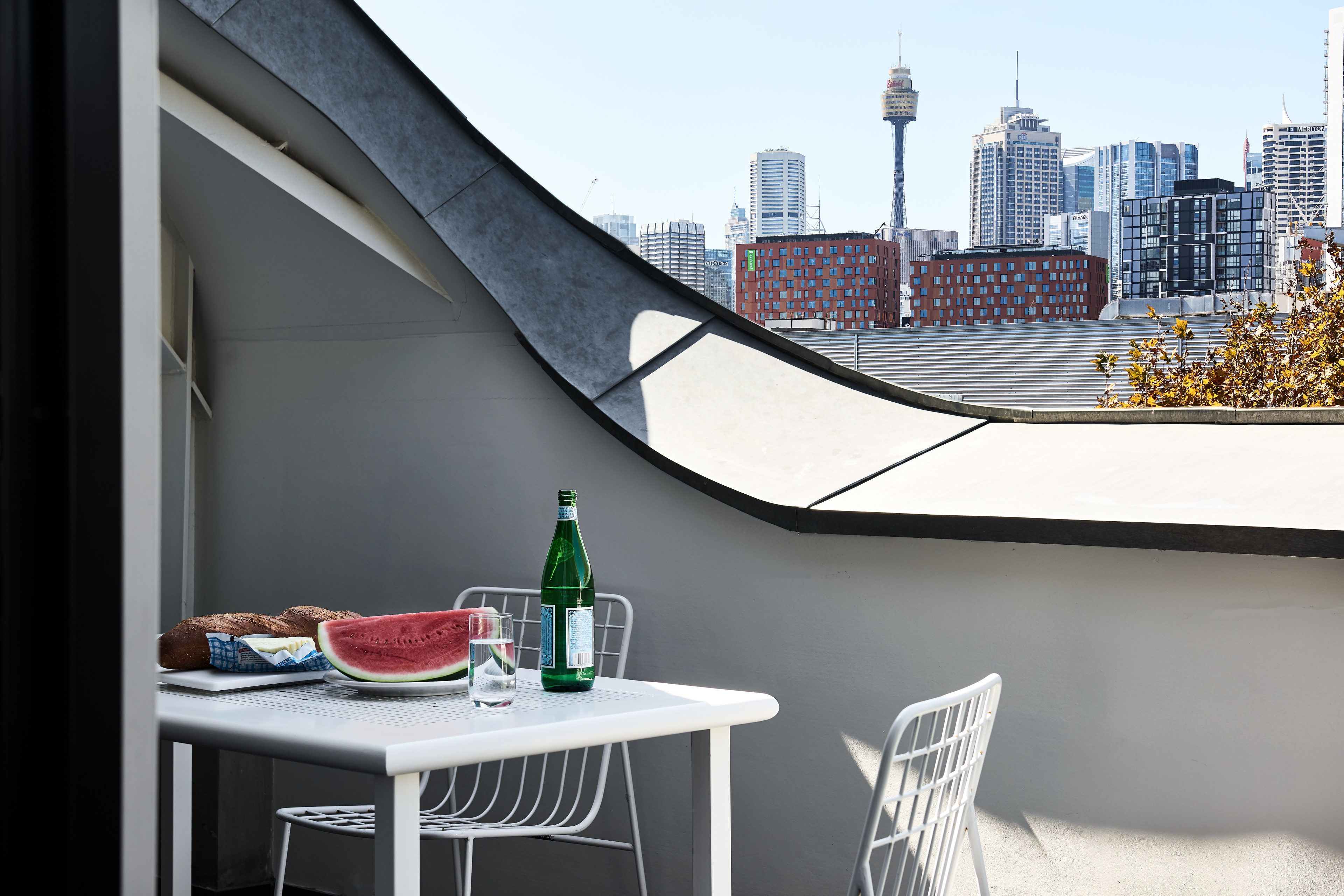 Un balcon avec une table, des chaises, une bouteille et une tranche de pastèque.