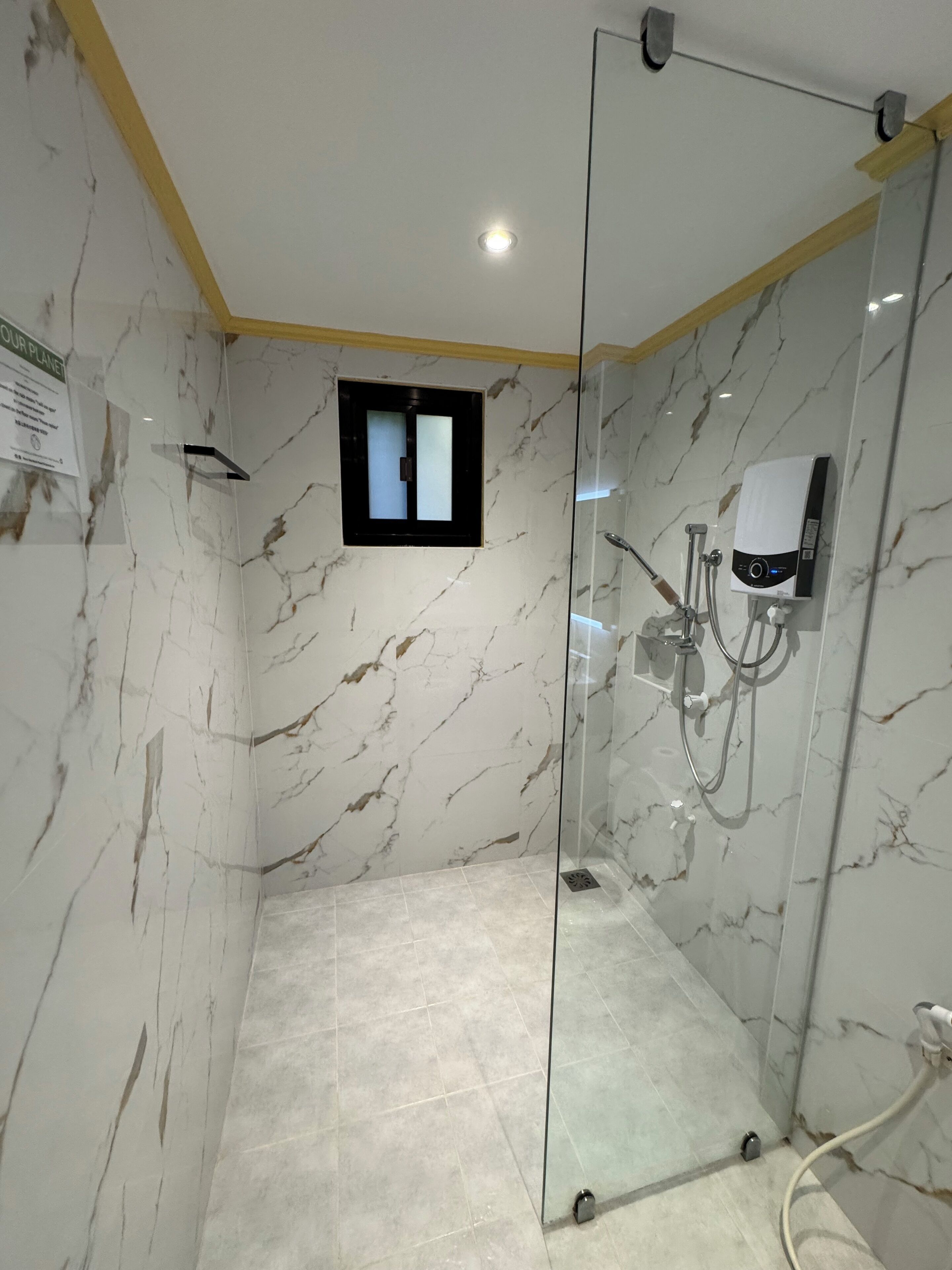 A glass-enclosed shower with a handheld showerhead, a wall-mounted faucet, and a control panel.