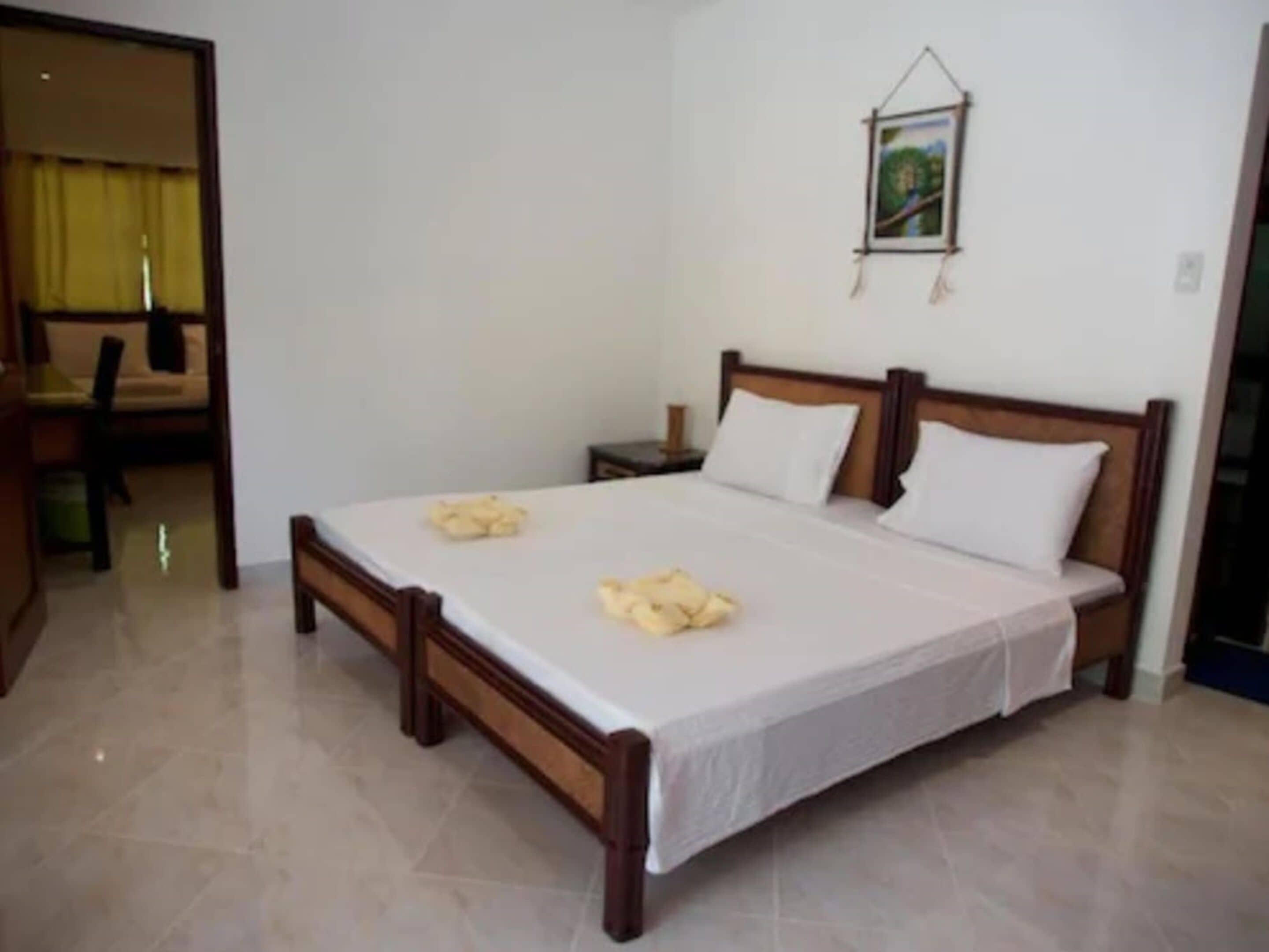 A bedroom with a wooden bed, white linens, a small bedside table, and a framed picture on the wall.