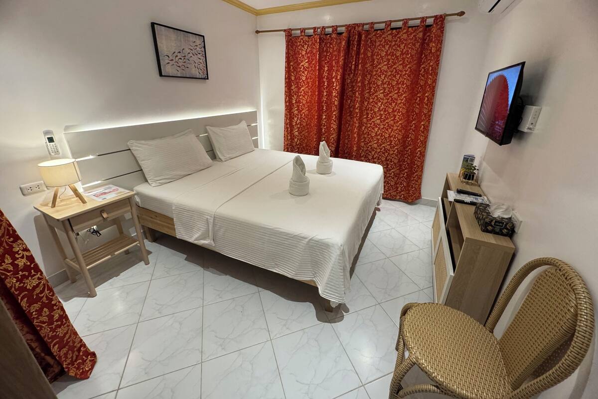 A hotel room with a bed, bedside table, lamp, TV, and a chair.