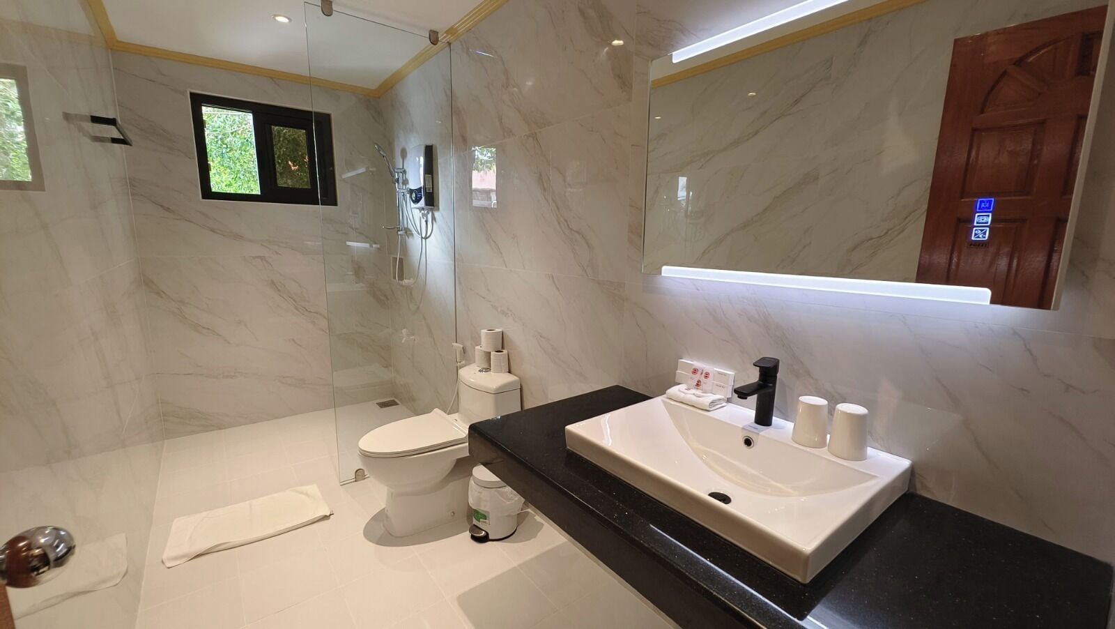 A modern bathroom with a glass-enclosed shower, a white toilet, and a black countertop with a sink and towel rack.