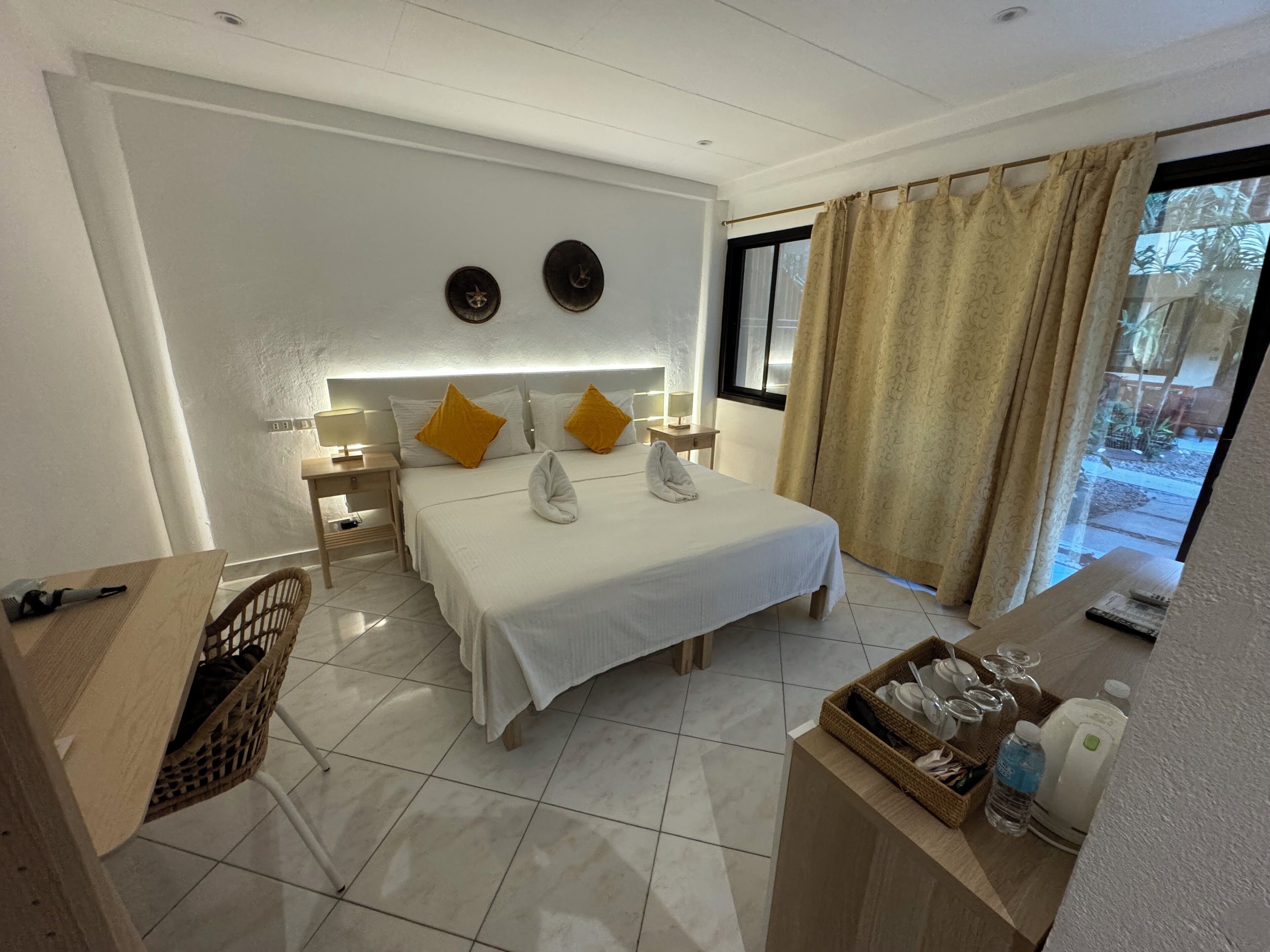 Camera d'albergo con un letto grande, due comodini con lampade, un tavolino con un cesto e vista all'esterno attraverso una finestra con tende.
