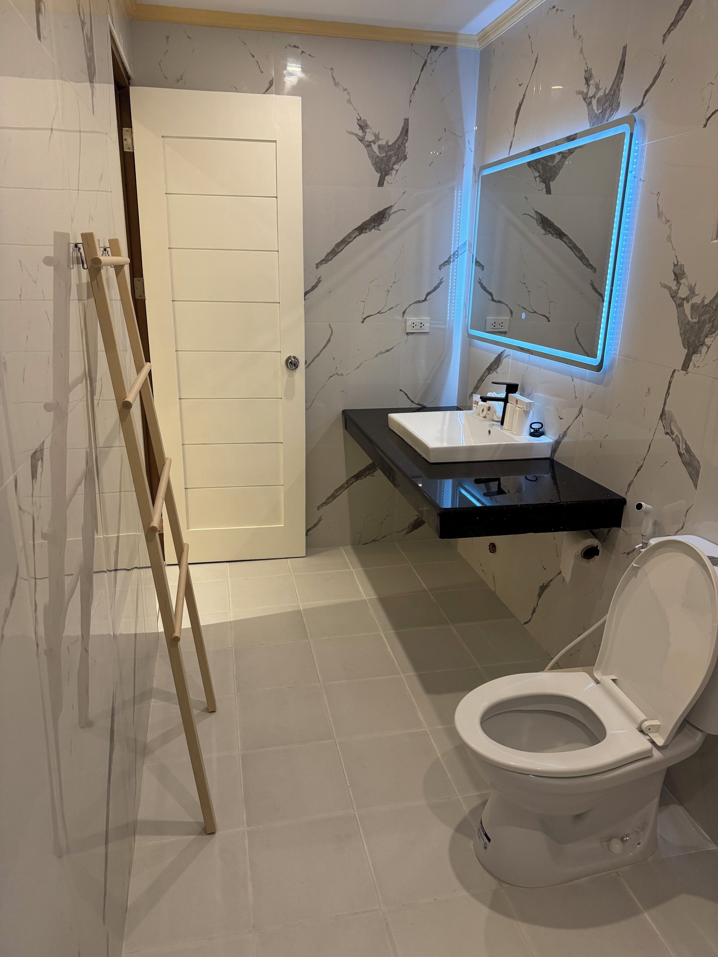 Een badkamer met een wit toilet, een zwarte wastafel met spiegel en een muur met een marmerlook.