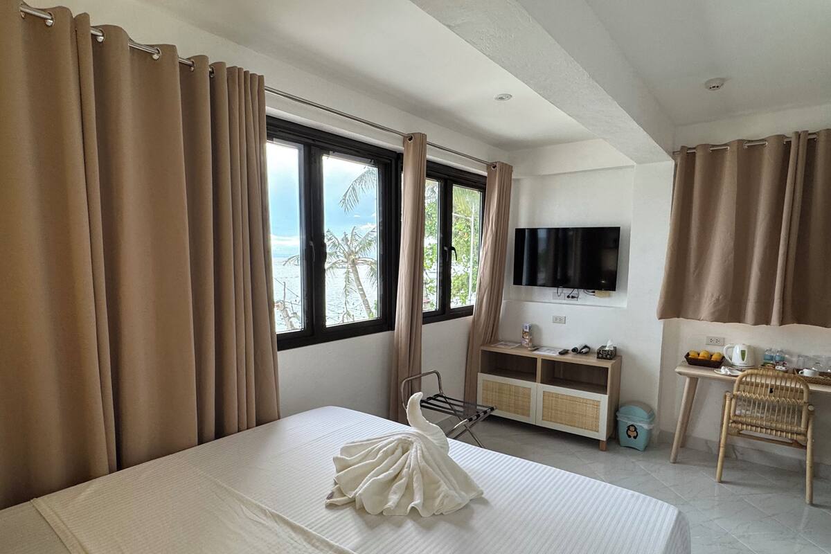 A hotel room with a bed, a TV, a small table with a chair, and a window with curtains.