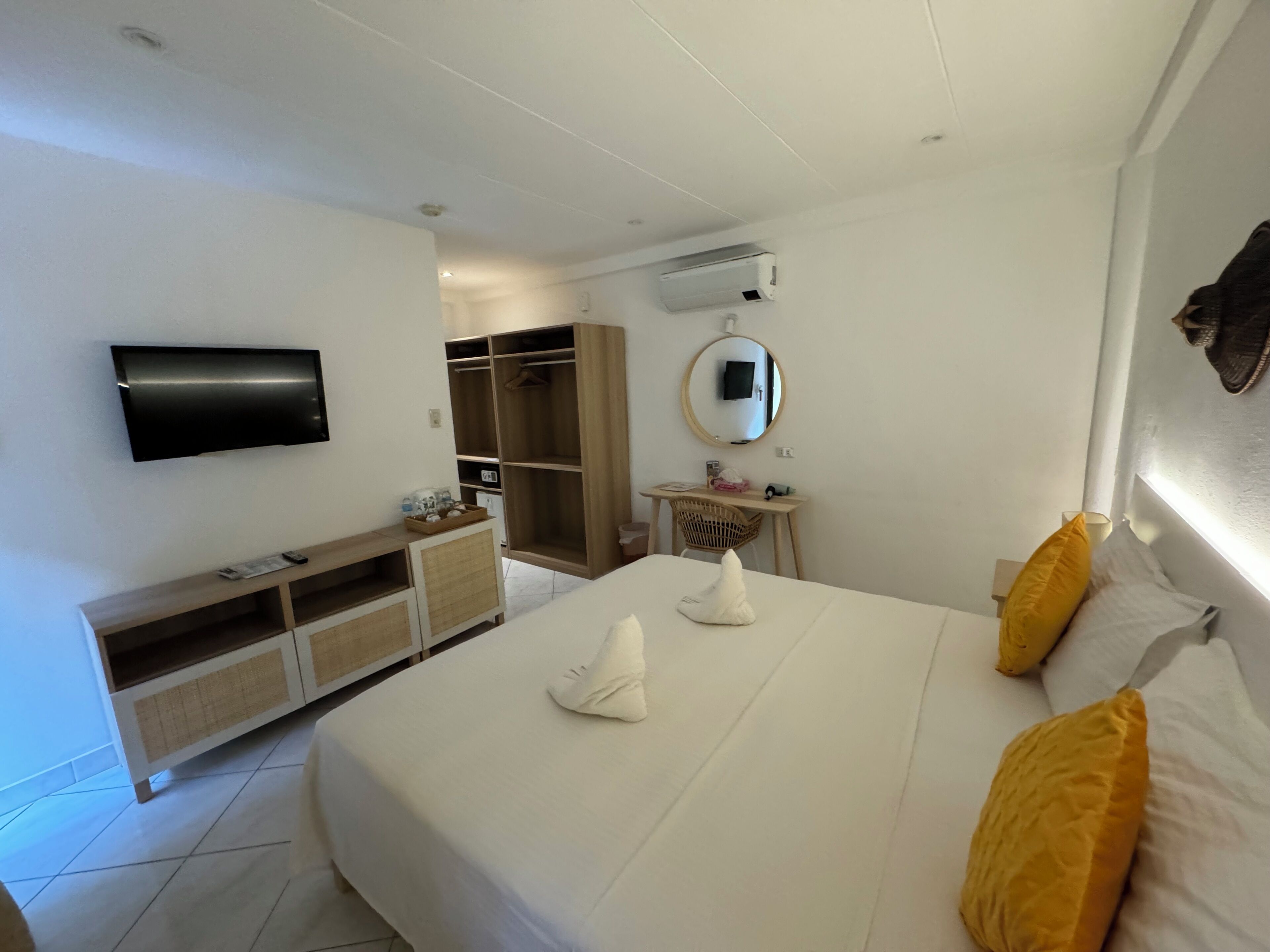 A hotel room with a bed, a desk, a wardrobe, a mirror, and a TV mounted on the wall.