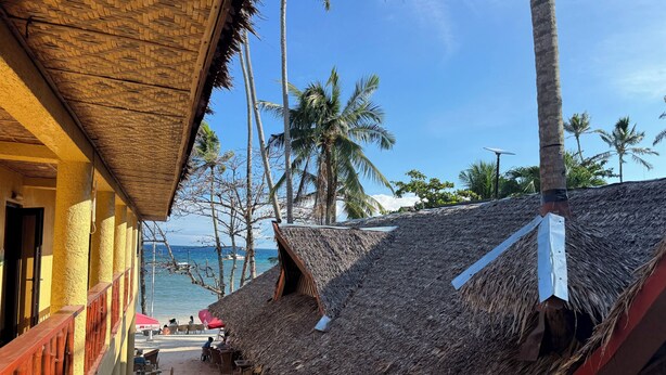 A beachside building with thatched roofs, outdoor seating, and a view of the ocean. - Alona Vida Beach Resort (Panglao)