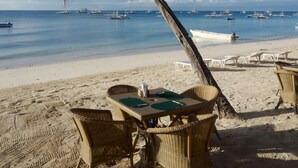 A beach with a table and chairs under a palm tree, overlooking the sea with boats. - Alona Vida Beach Resort (Panglao)