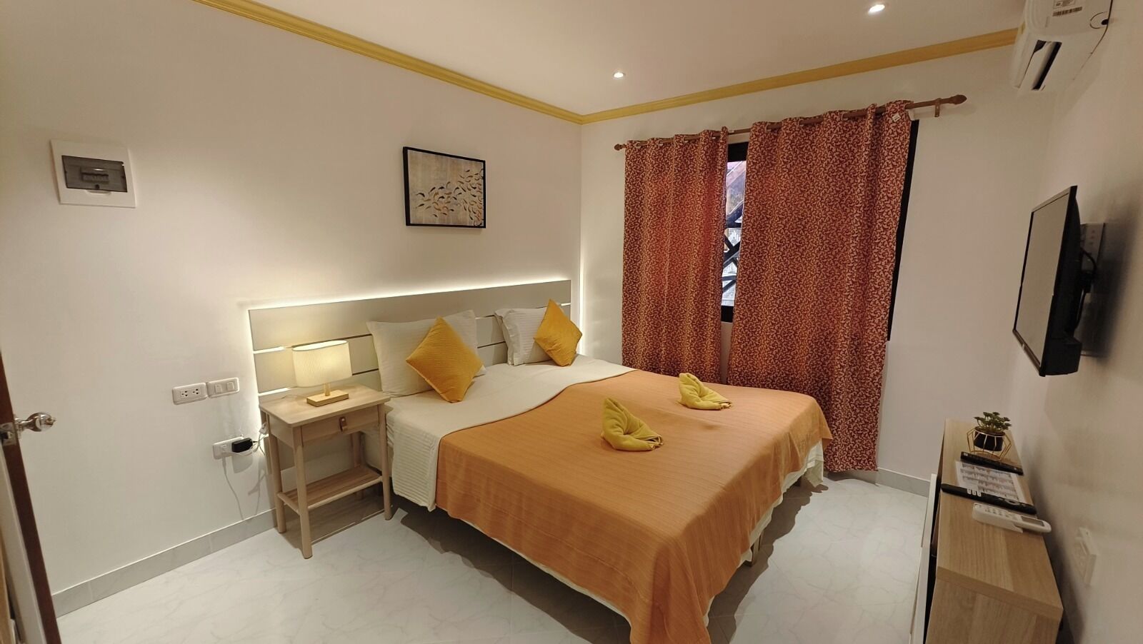 A hotel room with a bed, bedside table, lamp, and a TV on the wall.